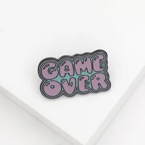 Detail of retro Game Over enamel pin with purple lettering on a green background