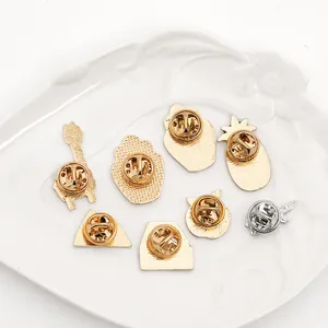 Detail view of various enamel pins with butterfly clutch backs on a white ceramic plate