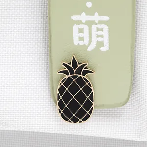Close-up of a cute pineapple enamel brooch with black drip oil finish on golden base