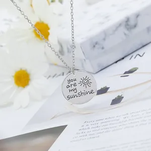 Gros plan du collier You Are My Sunshine avec pendentif soleil argenté sur marbre