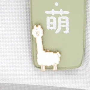 Detailed macro view of a cute white alpaca enamel brooch with gold metallic trim accents