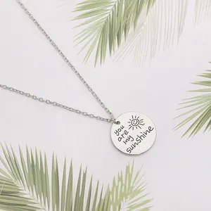 Détail macro du pendentif soleil gravé avec You are my sunshine sur du métal poli