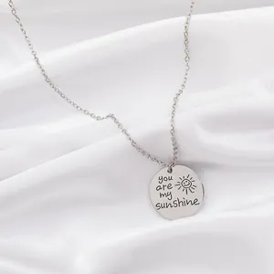 Détail macro du pendentif soleil gravé You are my sunshine sur fond de soie blanche