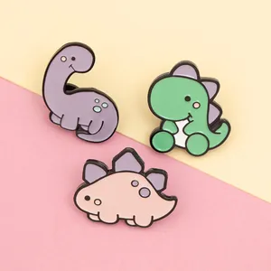 Three cute cartoon dinosaur enamel pins in purple green and pink colors on bright background