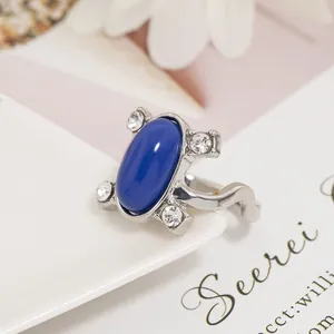 Dettaglio dell'anello con zaffiro blu ovale e cristalli scintillanti su un piatto bianco
