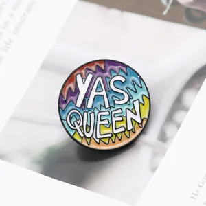 Round Yas Queen enamel pin with rainbow stripes and black metal finish on a book