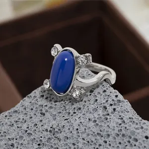 Dettaglio anello con zaffiro blu ovale e fascia ondulata su pietra vulcanica