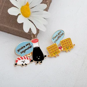 Vista dettagliata delle spille smaltate sushi e waffle kawaii su sfondo in tessuto bianco