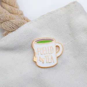 Macro shot of a Fueled by Tea enamel pin attached to a white canvas bag with gold edges