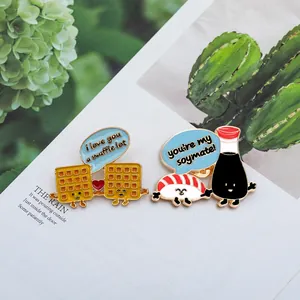 Dettaglio di spille in smalto kawaii con sushi e waffle su una pagina di rivista