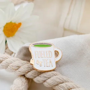 White enamel teacup brooch with Fueled by Tea quote and green tea detail on fabric