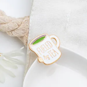Detailed view of Fueled by Tea enamel pin pinned on a white canvas bag