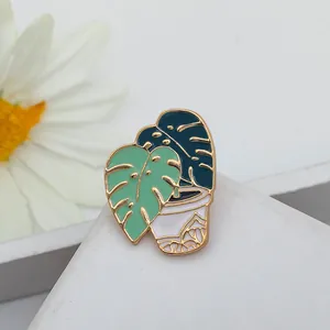 Macro shot of an enamel monstera plant brooch with green leaves in a white pot