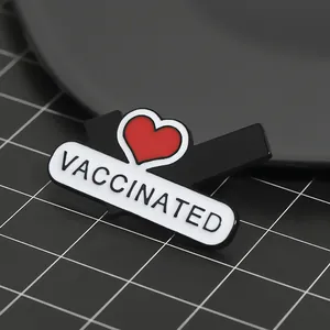 Macro shot of an enamel pin featuring a red heart and the word VACCINATED in bold text