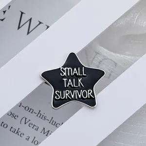 Detail view of a black Small Talk Survivor star pin on magazine pages and soft fabric