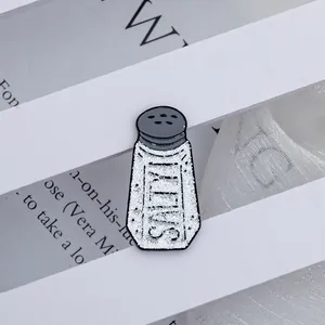 Macro shot of an enamel salt shaker pin with glittery white texture and Salty lettering