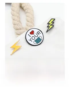 Detail of personalized enamel pins with lightning and heart icons on a white canvas bag