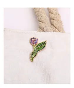 Detail view of purple tulip enamel brooch pinned on a white canvas bag accessory