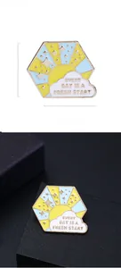 Macro detail of enamel hexagon brooch with sunrise scene and motivational quote text