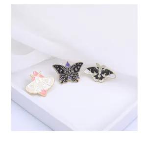 Détail de trois broches artistiques en émail motif papillon et mite sur plateau blanc