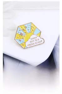 Detail of hexagonal enamel pin with sun and clouds and motivational slogan