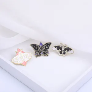 Trois pin's en émail céleste avec détails de lune et d'étoiles sur fond de tissu blanc