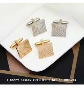 Macro shot of gold and silver square cufflinks with geometric sunburst texture on a tray