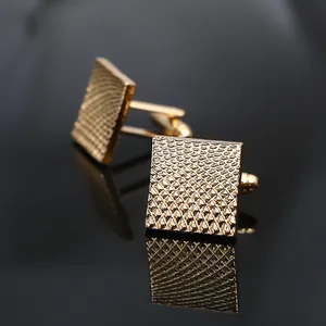 French style gold square cufflinks with textured grid pattern on black reflective surface