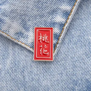 Detailed close-up of red enamel brooch with Peach Blossom text on denim fabric