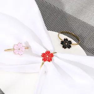 Detailed view of three cherry blossom napkin rings in pink, red, and black enamel on a table