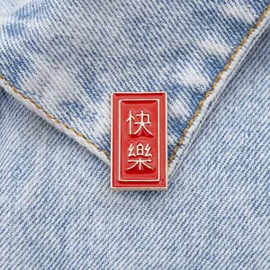 Detail of red enamel Happy brooch with silver Chinese text on blue denim fabric