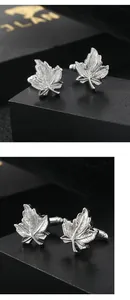 Macro shot of silver leaf cufflinks with detailed leaf vein textures on a black background
