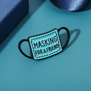 Blue face mask enamel pin featuring MASKING FOR A FRIEND slogan on a gift box