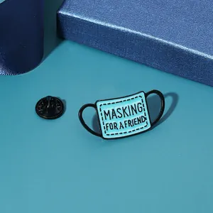 Enamel mask brooch featuring MASKING FOR A FRIEND quote on a blue textured background