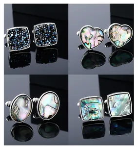 Macro view of square and heart-shaped abalone shell cufflinks on black mirror surface