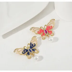 Détail de broches papillon avec ailes en émail et perle blanche suspendue élégante
