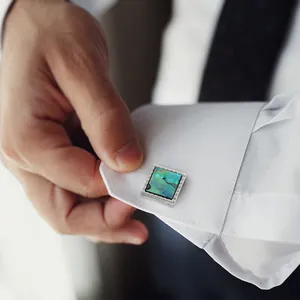 Square silver cufflinks with iridescent teal inlay on a white shirt sleeve cuff
