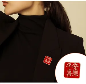 Détail d'une broche carrée rouge avec calligraphie blanche sur un veston