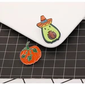 Gros plan de broches émaillées avocat et citrouille sur une assiette en céramique blanche
