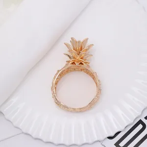 Close-up of golden pineapple napkin ring with textured metal finish on white ceramic plate