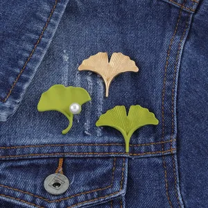 Elegant ginkgo leaf brooch set in gold and green metal pinned on a denim jacket