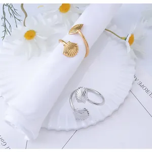 Detail of gold and silver shell napkin rings on white fabric with elegant ceramic plates