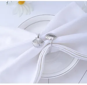 Close-up of a silver shell-shaped napkin ring on a white napkin over a ceramic plate