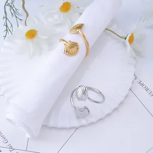 Shell-shaped napkin rings with fan texture in gold and silver finish on a ceramic plate