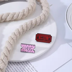 Detail van rode Hell Admit One en roze 1 Hug emaille pinnen op een wit bord