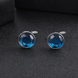 Close-up of silver round cufflinks featuring faceted blue crystals on black leather texture