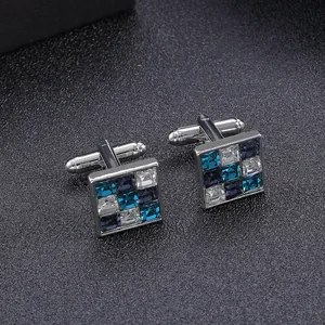 Close-up of square silver cufflinks with blue and clear zircon stones on grey leather