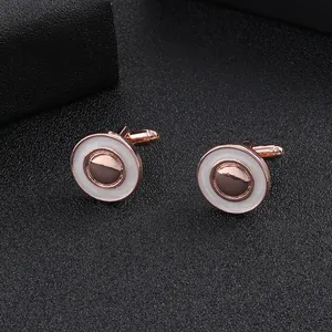Détail de boutons de manchette ronds or rose avec émail blanc sur fond de cuir sombre