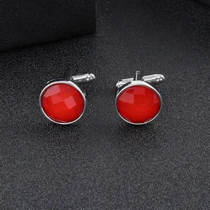 Close-up of polished silver cufflinks with round faceted red gemstones on grey texture