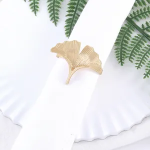 Detalle de servilletero dorado hoja de ginkgo con perlas sobre servilleta blanca